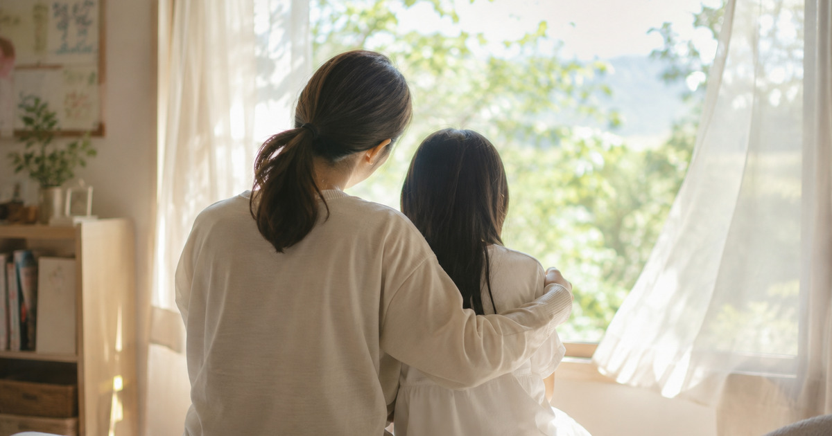 窓辺で寄り添う母と子の後ろ姿